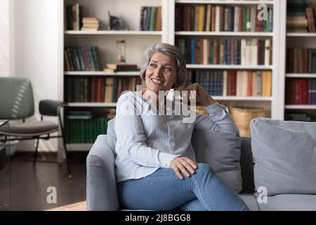Une heureuse femme de 60s ans assise sur un canapé confortable dans la salle de séjour Banque D'Images