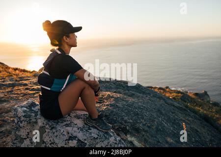 Femme de sport profitant du coucher de soleil. Randonneur féminin assis sur le rocher et regardant à distance. Banque D'Images