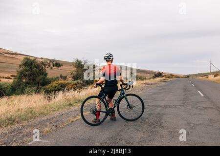 Vue arrière d'une cycliste professionnelle assise sur son vélo de route pour se détendre après l'entraînement Banque D'Images