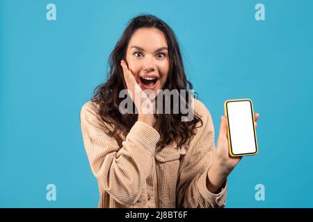 Joyeuse excitée jeune européenne brune dame dans une ambiance décontractée avec la bouche ouverte appuie main à joue, montre téléphone Banque D'Images