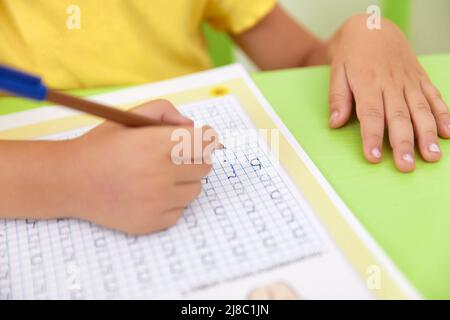 Main de l'enfant tenant le crayon et étudier avec le numéro d'écriture d'apprentissage sur le livre papier à l'école ou à la maternelle et à la crèche Banque D'Images