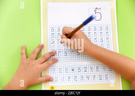 Main de l'enfant tenant le crayon et étudier avec le numéro d'écriture d'apprentissage sur le livre papier à l'école ou à la maternelle et à la crèche Banque D'Images