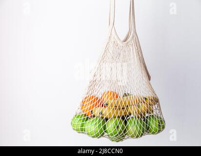 Sac à ficelle blanche avec pommes vertes, oranges et bananes sur fond blanc. Banque D'Images