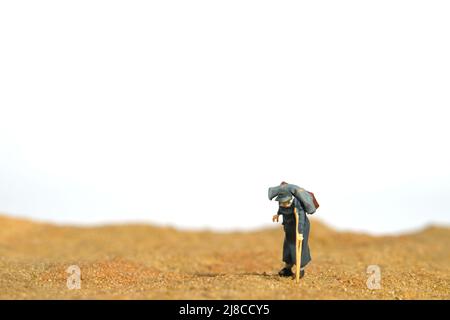 Photographie miniature de personnage de jouet de personnes. Un vieux grand-père d'hommes marchant seul dans le désert, se déplaçant dans le camp de réfugiés en raison d'un conflit de guerre. PH de l'image Banque D'Images