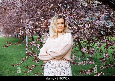 Portrait de belle femme blonde de cheveux avec un maquillage doux et des boucles parfaites posant sur fond lilas en fleur dans des vêtements décontractés roses. Mode Banque D'Images