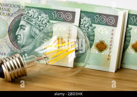 Ampoule et monnaie polonaise, billets de 100 PLN chacun, le concept des prix de l'énergie et de l'électricité devenant plus coûteux avec l'inflation croissante Banque D'Images