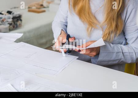 La couturière coupe des motifs de paper pour la robe avec des ciseaux. Développement de conception et création de vêtements Banque D'Images