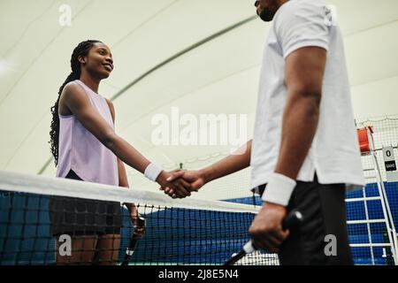 Tir en contre-plongée de deux joueurs de tennis qui se secouent les mains sur le filet pendant le match sur un court en salle