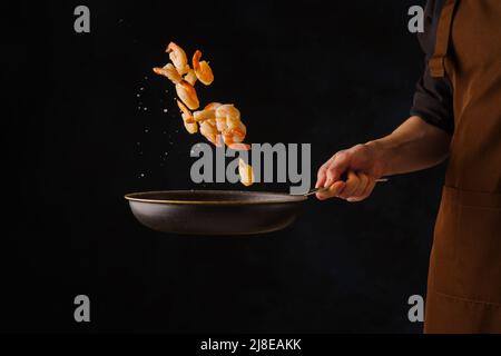 Des crevettes géantes dans une poêle en vol gelé sur fond noir dans la main du chef. Recettes pour cuisiner des plats à base de fruits de mer et de crevettes. Restaurant, Banque D'Images