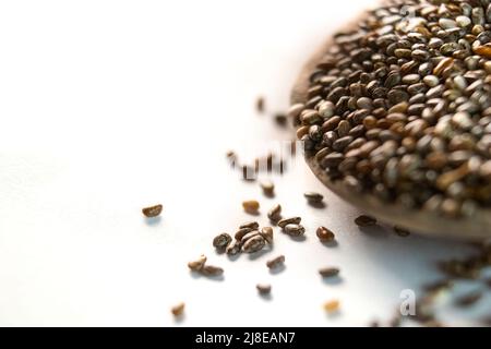 Un tas de graines de chia organique sur une cuillère en bois riche en acides gras oméga-3, vue latérale sur fond blanc Banque D'Images