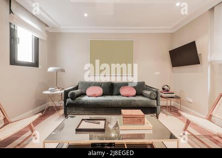 Salon avec canapé en velours vert, coussins rouges, table d'appoint et miroir en métal doré, tv au mur et chaises en bois et osier Banque D'Images
