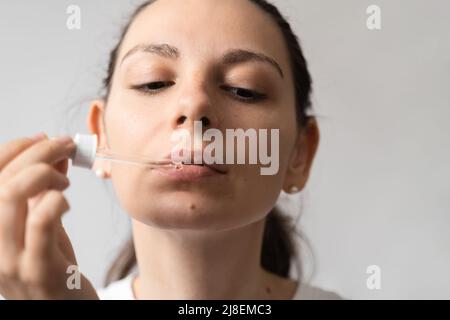 Portrait de la jeune femme aux cheveux foncés prenant un supplément d'huile avec un compte-gouttes en verre. CBD huile de médecine de chanvre appliquée sur la langue Banque D'Images