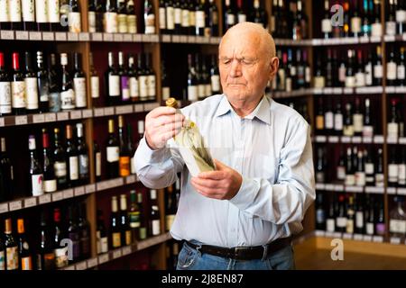 Le retraité confiant choisit le vin blanc dans un magasin de spiritueux Banque D'Images