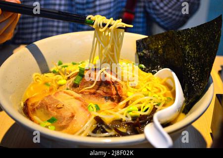 Les baguettes ramassent le tonkotsu ramen japonais avec l'algue, le porc (tonkotsu), le germe de haricots et les échalotes dans un bol. Banque D'Images