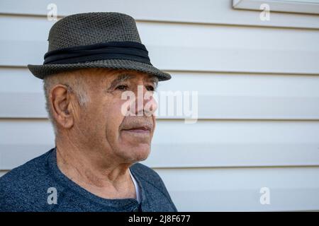 homme caucasien adulte âgé avec un chapeau fedora devant un mur extérieur de maison blanche Banque D'Images