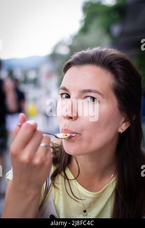 Une jeune femme mangeant une crème brûlée à l'extérieur dans un restaurant, un concept de vacances et de profiter de l'été. Photo verticale. Banque D'Images