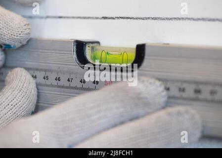Les mains du travailleur vérifient la planéité du mur à l'aide d'un outil spécial pour mesurer le niveau. La scène de face au mur de la cuisine avec des carreaux de céramique blanche Banque D'Images
