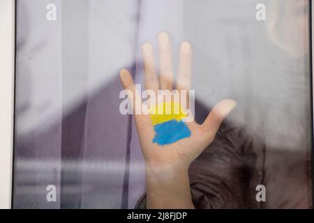 La main d'une fille dans la fenêtre de sa maison avec un drapeau jaune-bleu peint de l'Ukraine, la paix en Ukraine, arrêter la guerre, une action de protestation et un patri Banque D'Images