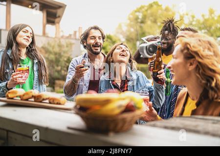 Des amis gaies se rassemblent au bar du kiosque sur la plage en écoutant de la musique avec une boombox, en riant, en buvant des bières, du vin, des cocktails - le style de vie des jeunes c Banque D'Images