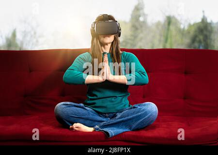 Femme en lunettes VR est assis dans une position de yoga de lotus joignant les mains - méditation virtuelle - fille prenant des cours de yoga dans la réalité virtuelle - style de vie et tec Banque D'Images