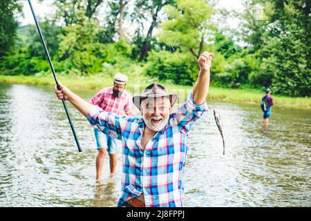 Portrait de l'homme senior gai de la pêche. Homme de pêche senior excité en chapeau de cow-boy avec canne à pêche, tournant le rabatteur sur la rivière. Vieil homme qui attrape du poisson Banque D'Images