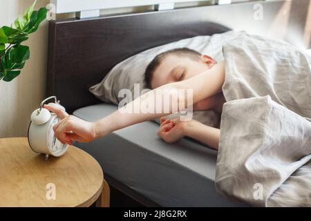 garçon allongé sur le lit et arrêtant le réveil le matin. les enfants se tournent vers le réveil pour l'éteindre. Banque D'Images