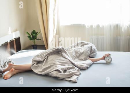 garçon allongé sur le lit sous une couverture et le réveil de l'arrêt le matin. main de childs se levant pour le réveil pour l'éteindre. Banque D'Images