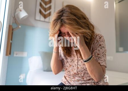 Femme âgée avec des douleurs au chevet assise sur le lit dans son appartement. Banque D'Images