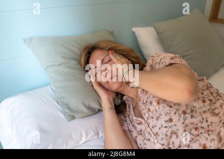 Femme âgée souffrant de maux de tête graves, couchée sur le lit de sa chambre. Banque D'Images