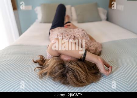 Femme aux maux de tête couchée sur le lit et avec son bras sur son visage. Banque D'Images