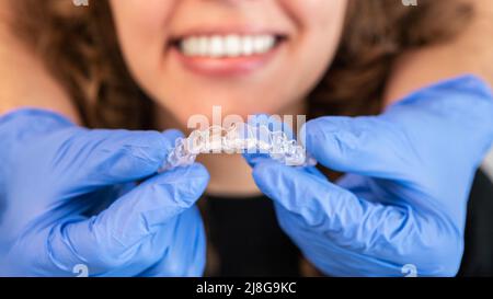 Orthodontiste médecin en gants en silicone invisible bretelles transparentes sur les dents de la femme dans la clinique de dentiste, vue rapprochée de la bouche. Correction des dents t Banque D'Images