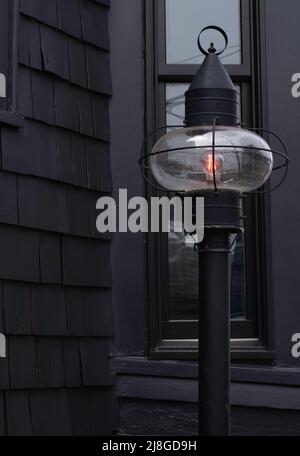 Lanterne de rue noire illuminée d'une lueur orange vif devant une maison noire avec fenêtre Banque D'Images