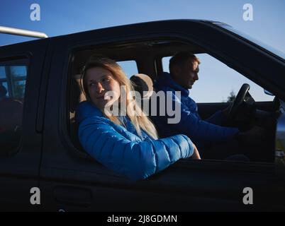 Petite passager, assis dans la cabine de la voiture noire avec son chauffeur de petit ami, regardant autour de la zone, se penchant sur la porte latérale de la voiture. Conduite par temps ensoleillé. Banque D'Images