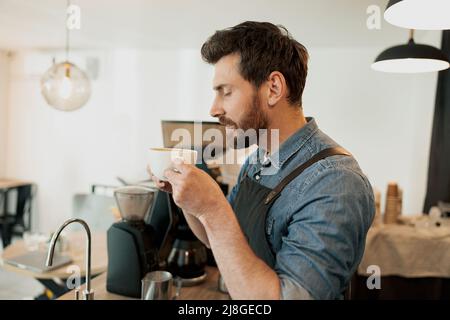 Un beau barista avec une barbe élégante qui sent le café à la cafétéria Banque D'Images