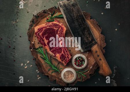 présentation esthétique de la planche à découper vintage avec du bœuf cru dessus, un couteau à laver, du poivre rouge et vert, du sel rose et du romarin d'une vie de haut Banque D'Images