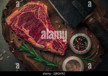 gros plan du steak rouge non cuit du haut du biew avec romarin, poivre coloré, sel rose et couteau à pince sur la planche à découper en bois d'époque Banque D'Images