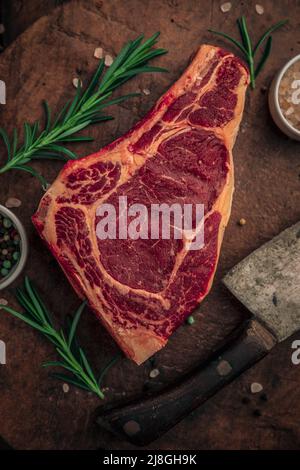 planche à découper vieille rouille avec steak de bœuf sur lui avec des herbes, petits bols de poivre coloré et sel rose avec un grand couteau à côté de lui et sprin Banque D'Images