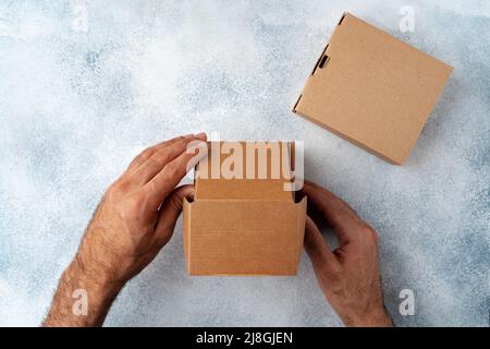 Boîte de carton dans un homme mains sur un fond de table gris Banque D'Images