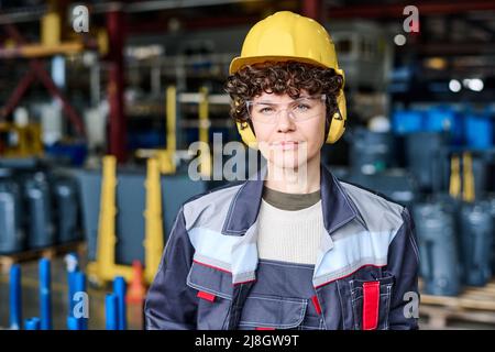 Jeune femme ingénieure confiante portant un uniforme, un casque, des lunettes de protection et un casque debout devant l'appareil photo Banque D'Images