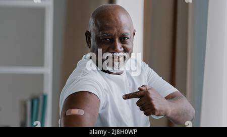 Portrait afro-américain ancien homme mature senior patient montre le plâtre médical sur l'épaule démontre la marque d'injection client mâle satisfait après Banque D'Images