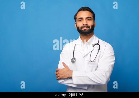 Médecin indien sérieux enfant, physique, thérapeute portant une blouse médicale blanche avec stéthoscope sur les épaules, bras croisés isolés sur bleu, espace de copie. Santé et médecine Banque D'Images