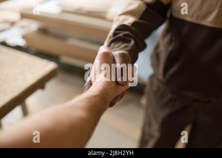 Gros plan de deux travailleurs manuels multiethniques qui se secouent la main pendant le travail d'équipe en usine Banque D'Images