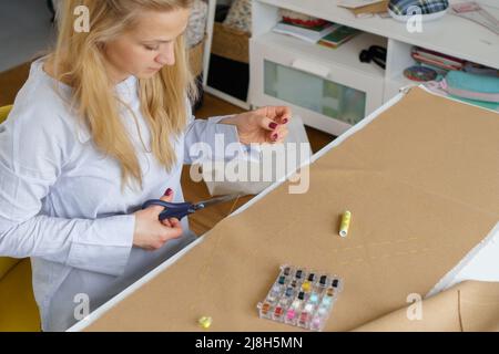 Tailleur avec aiguille dans les mains en coupant le fil avec des ciseaux . Femme couturière sur le lieu de travail. Travaux d'aiguille Banque D'Images