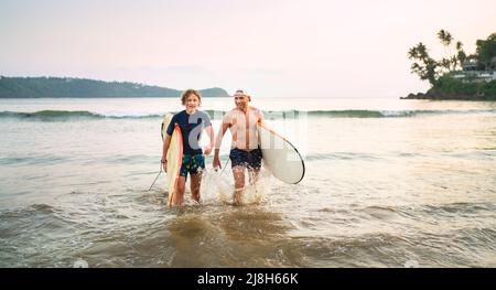 Portrait d'un jeune garçon avec son père avec des planches de surf après le surf.Ils sourient et sortent de l'eau.Vacances actives en famille ou actives Banque D'Images