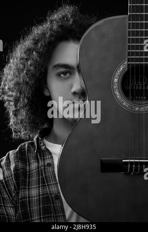 Un jeune homme aux cheveux bouclés pose avec une guitare acoustique devant son visage. Photo en noir et blanc. Photo de haute qualité Banque D'Images