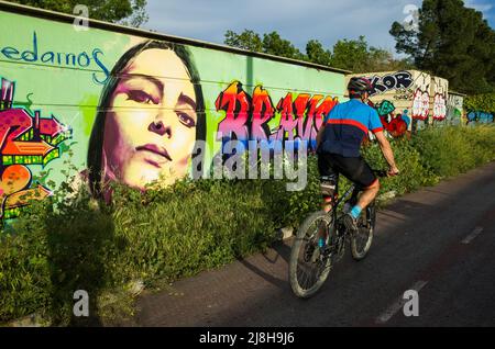 Grenade, Andalousie, Espagne : Un cycliste sur le bikeway passe devant la peinture murale graffiti de l'artiste de rue El niño de las pinturas. Banque D'Images