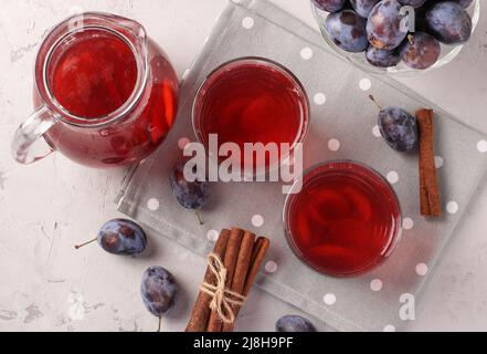 Compote de prunes en verseuse et deux verres sur fond gris, vue du dessus Banque D'Images