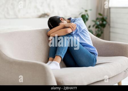 Vue latérale d'une femme asiatique assise sur un canapé, pleurant Banque D'Images