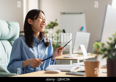 Femme asiatique souriante jouant à la batterie virtuelle au travail Banque D'Images