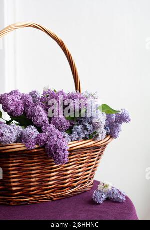 Un panier en bois avec un énorme bouquet coloré de lilas se dresse sur une table recouverte d'une nappe pourpre Banque D'Images